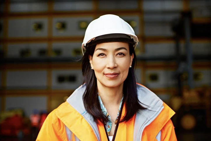 Female lone worker smiling at camera wearing a high visibility jacket and protective gear